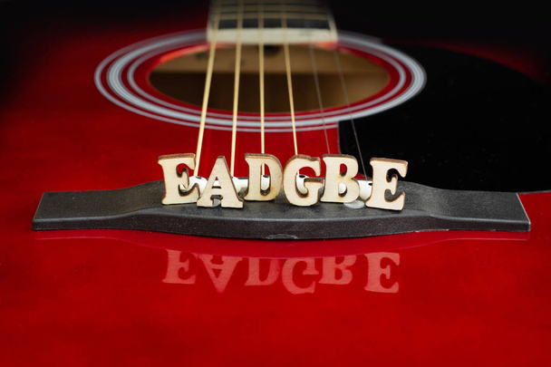 Nuty muzyczne Eadgbe odpowiadające aranżacji ciągów, z drewnianymi literami, na mostku gitary akustycznej. Perspektywa mostu gitary. Kreatywne tło. - Zdjęcie, obraz