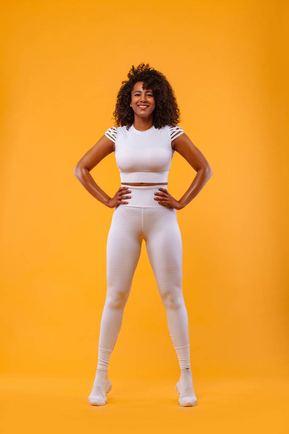 Smiling strong athletic woman with black skin and curly hair, doing exercise on yellow background wearing sportswear. Fitness and sport motivation. - Foto, Imagem