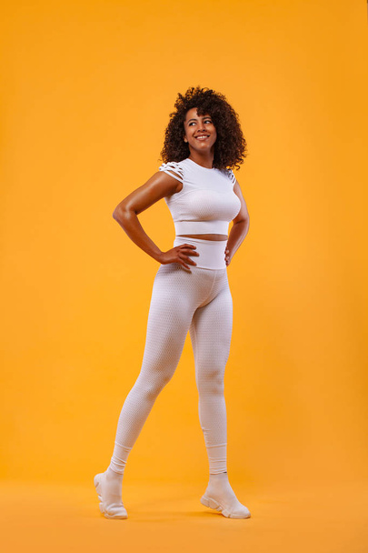 Smiling strong athletic woman with black skin and curly hair, doing exercise on yellow background wearing sportswear. Fitness and sport motivation. - Fotografie, Obrázek