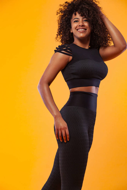 Lifestyle Concept. Portrait of beautiful African American woman with curly hair joyful listening to music on mobile phone. Yellow studio background. Copy Space. - Photo, image