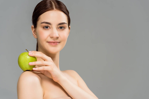 cheerful nude woman smiling while holding green apple isolated on grey  - Foto, immagini
