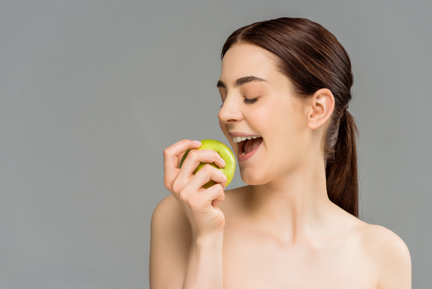  happy woman holding green apple near open mouth isolated on grey  - Foto, immagini