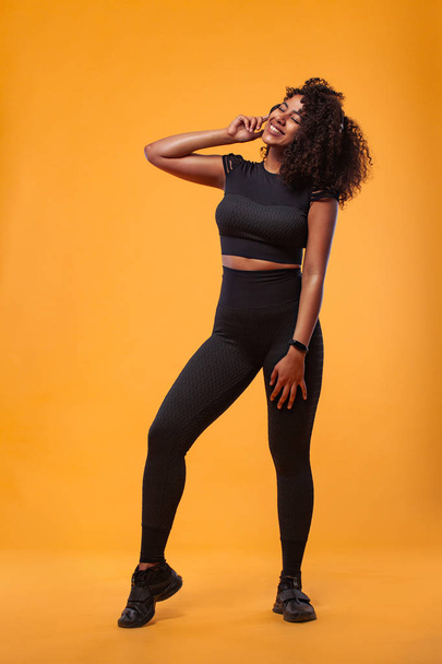 Lifestyle Concept. Portrait of beautiful African American woman with curly hair joyful listening to music on mobile phone. Yellow studio background. Copy Space. - Foto, immagini