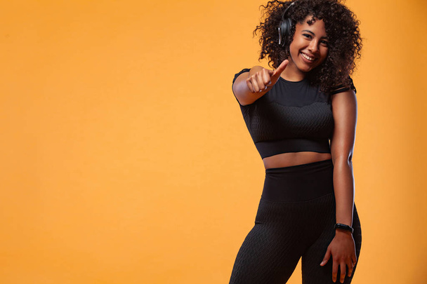 Lifestyle Concept. Portrait of beautiful African American woman with curly hair joyful listening to music on mobile phone. Yellow studio background. Copy Space. - Foto, Imagem