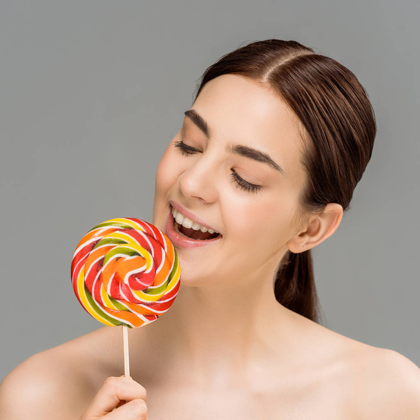 cheerful naked woman looking at colorful lollipop isolated on grey  - Fotó, kép