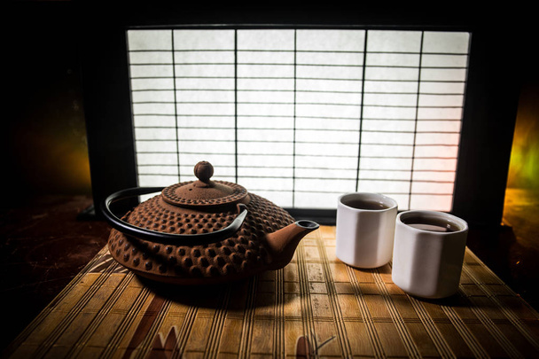 Tea concept. Japanese tea ceremony culture east beverage. Teapot and cups on table with bamboo leaves on sunset - Photo, Image