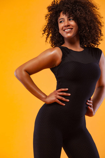Smiling strong athletic woman with black skin and curly hair, doing exercise on yellow background wearing sportswear. Fitness and sport motivation. - Foto, Imagem
