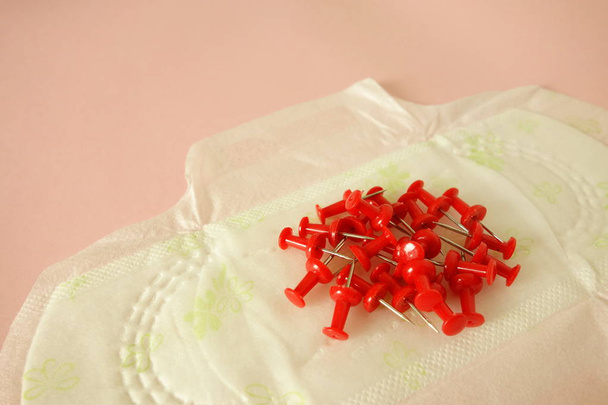 Bloc menstruel avec broches rouges sur fond rose, vue rapprochée
 - Photo, image
