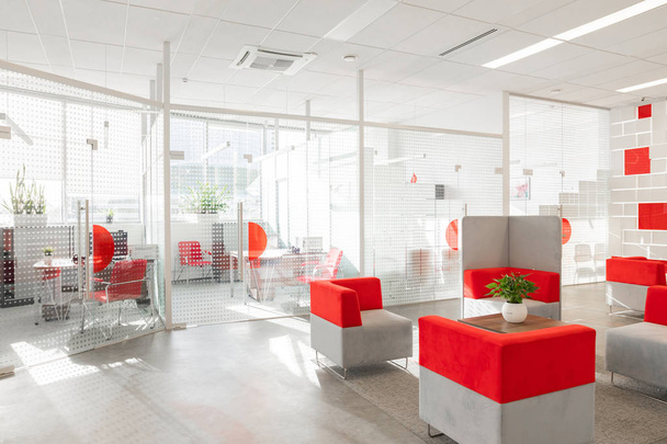 Minsk, Weißrussland - 23. Mai 2019: Ecke modernes Büro mit weißen Wänden, grauem Boden, Freifläche mit rot-weißen Sesseln und Räumen hinter Glaswand - Foto, Bild