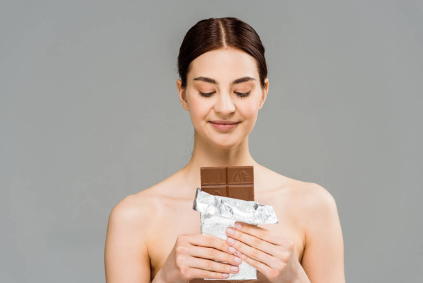 весела молода жінка дивиться на шоколадний батончик ізольовано на сірому
  - Фото, зображення