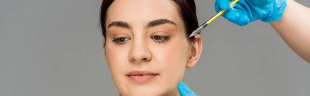 πανοραμική βολή πλαστικού χειρουργού που κάνει ένεση ομορφιάς σε γυναίκα απομονωμένη σε γκρι  - Φωτογραφία, εικόνα
