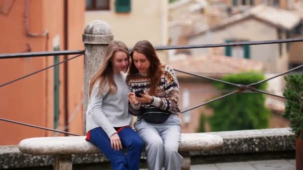 İki genç kadın bankta oturuyor ve elde edilen fotoğrafları izlemek ve gülmek. - Video, Çekim
