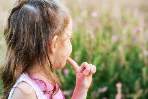 Menina bonito olha para trás ao ar livre no campo verde. Retrato infantil
 - Foto, Imagem