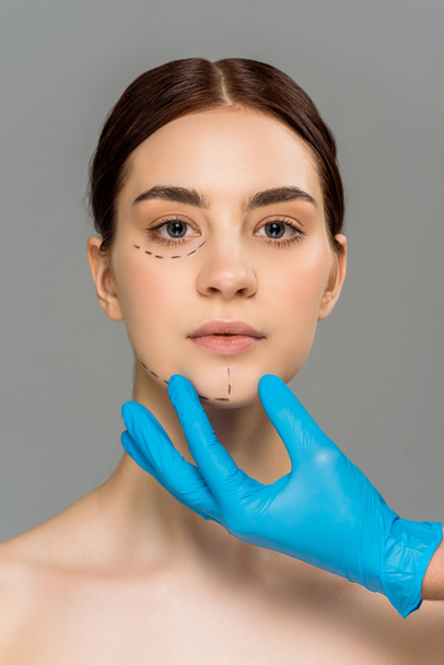 vista recortada de cirujano plástico en guante de látex tocando la cara de mujer desnuda atractiva aislada en gris
  - Foto, imagen