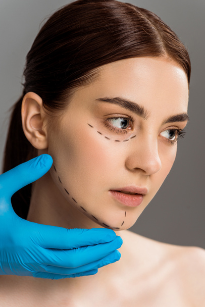 cropped view of plastic surgeon in latex glove touching face of pretty naked woman isolated on grey  - Fotoğraf, Görsel