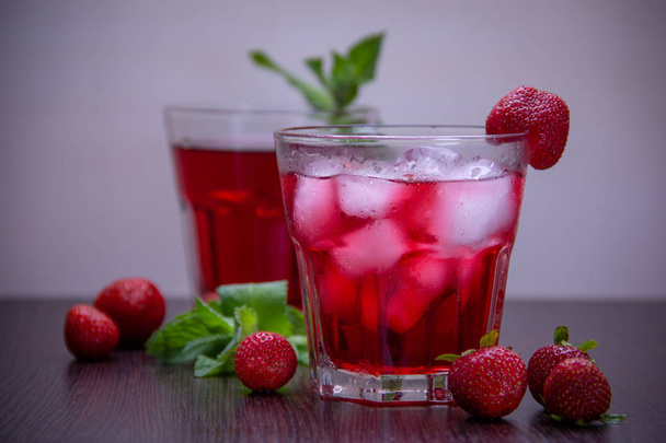 Two glasses with a red drink and ice are on the table, ripe strawberries and an aromatic mint branch are nearby. - Photo, Image