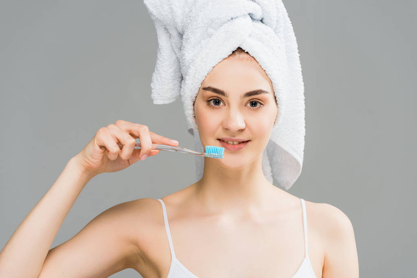attractive young woman with towel on head holding toothbrush isolated on grey  - 写真・画像