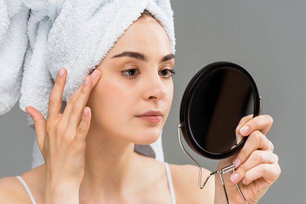 attractive young woman with towel on head looking at mirror isolated on grey  - Photo, image