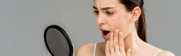 panoramic shot of shocked woman with acne on face looking at mirror isolated on grey  - Foto, immagini