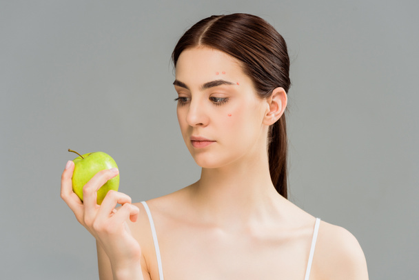 mujer joven con acné mirando manzana verde aislada en gris
  - Foto, Imagen