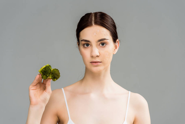 brunette woman with face scrub holding green broccoli isolated on grey  - Fotografie, Obrázek