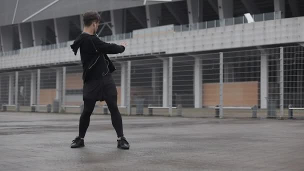Attractive male athlete does morning exercise outdoors close up slow motion in the cloudy weather. Workout standing on the street near sports stadium. Healthy lifestyle will power motivation concept. - Filmati, video