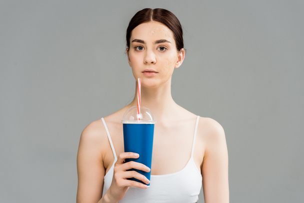 young brunette woman with problem skin holding plastic cup isolated on grey  - 写真・画像