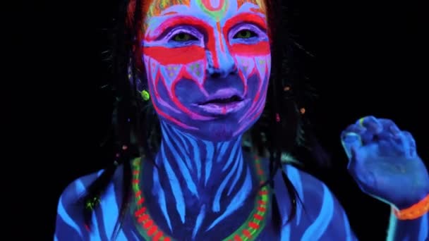 Zbliżenie portret młodych adorable bodyarted dziewczyna w ultrafioletowe światło na czarnym tle. Czarny światło świecące farby body art avatar Cosplay Lady z barwione emocjonalne twarz - Materiał filmowy, wideo