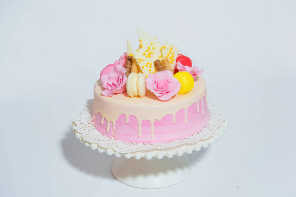 白い背景にピンクのケーキ。ピンクの釉薬にチョコレートと色のマカロンケーキの作品で飾られた甘いペストリーは、スタンド上にあります. - 写真・画像