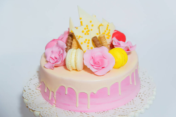 Pastel rosa sobre fondo blanco. Pastelería dulce decorada con trozos de chocolate y macarrones de colores Pastel en esmalte rosa está en el soporte
. - Foto, Imagen