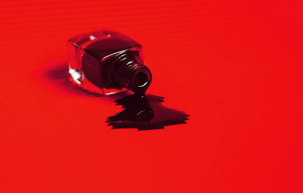 Dark nail polish spilled from the bottle. Vibrant red background. - Zdjęcie, obraz