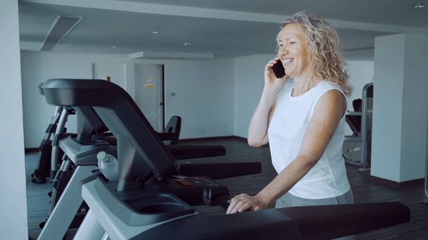 senior woman doing treadmill in the gym and talking on the phone - Foto, immagini