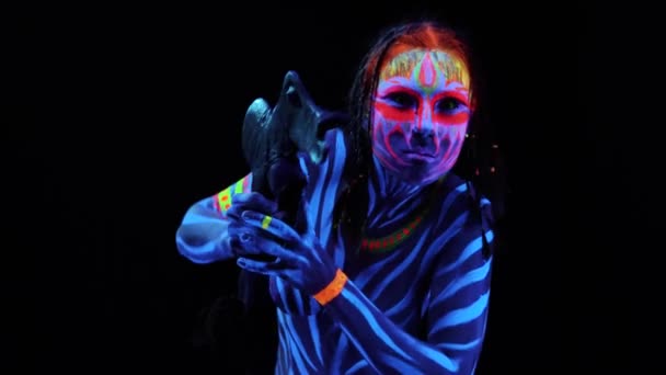 Retrato de una joven mujer salvaje desnuda con cuerpo en pintura ultravioleta azul brillante con arma tomahawk prehistórica primitiva. Agresivo avatar guerrero amazon con pigtails peinado
 - Imágenes, Vídeo