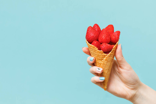 Waffle cone with strawberries  in female hand. Fresh summer fruits. - Foto, afbeelding