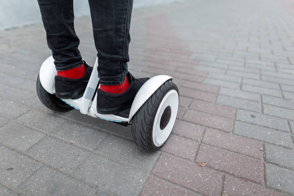 Men's legs in black jeans in red vintage socks in fashionable black sneakers on a gyroscope on a summer day. Modern guy stands on a hoverboard outdoors in the city. Close-up. - Photo, Image