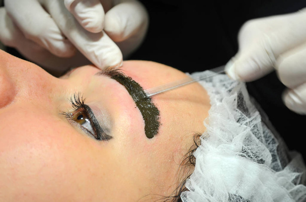 Dziewczyna z makijażu leżącego na procedurze mikroblading. Kosmetolog sprawia, że Makijaż permanentny na brwi. - Zdjęcie, obraz