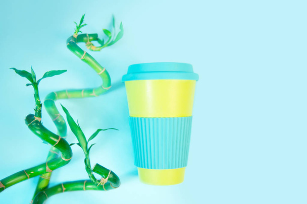 Zero waste concept. Stylish reusable eco coffee cup and green bamboo leaves. - Fotó, kép
