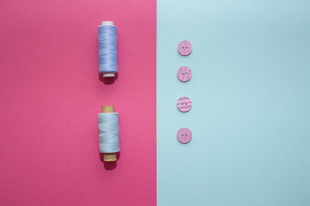 Composición con hilos azules y accesorios de costura sobre fondo rosa. Botones rosados sobre fondo azul. Pisos, lugar para el texto
 - Foto, imagen