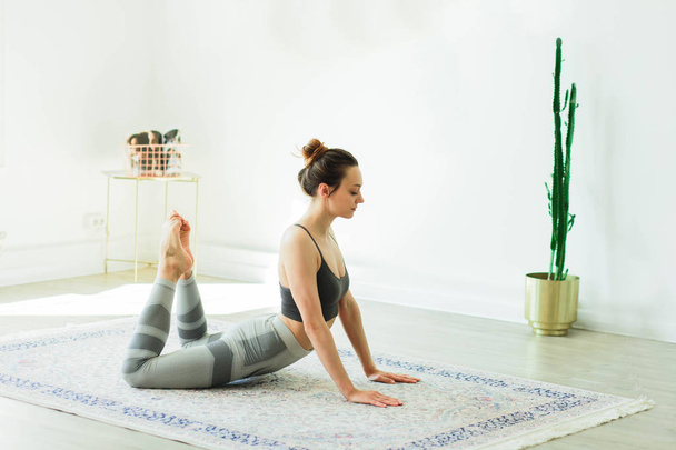 junge schöne lächelnde Frau praktiziert Yoga in einem hellen Raum - Foto, Bild