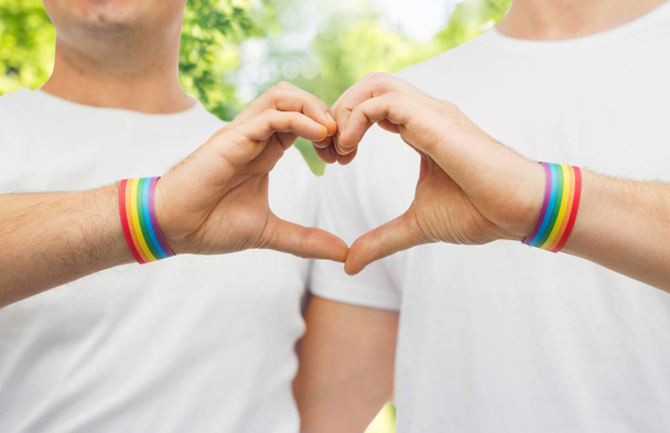 Schwules Paar mit Regenbogenarmbändern und Handherz - Foto, Bild