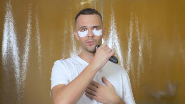 Portrait of a handsome man with an eye mask that shaves with an electric razor in the bathroom. Metrosexual concept - Foto, imagen