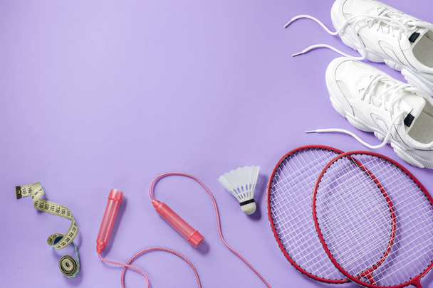 Sport equipment. Shuttlecock and badminton racket, skipping rope, sneakers and measuring tape on purple background. Fitness, sport and healthy lifestyle concept.Flat lay, top view, copy space - Фото, изображение