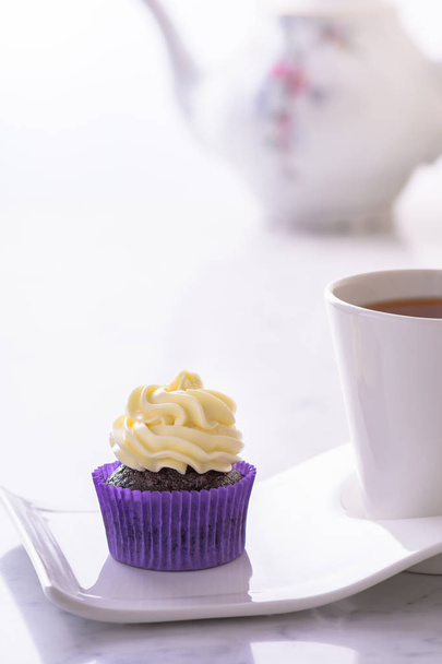 Cupcake in purple wrap and a cup of tea on white natural marble table top with copy space. - Φωτογραφία, εικόνα