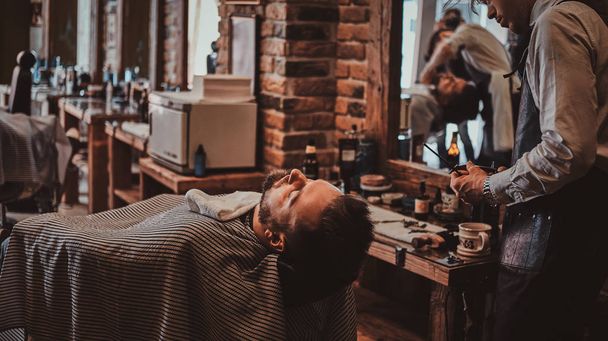 Thendy hairdresser at modern barbershop is working on clients haircut. - Foto, afbeelding