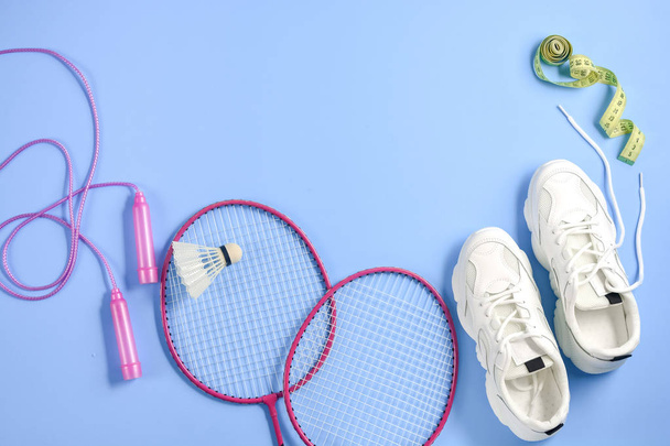 Sports flat lay with shuttlecock and badminton racket, skipping rope, sneakers and measuring tape on purple background. Fitness, sport and healthy lifestyle concept. - Photo, image