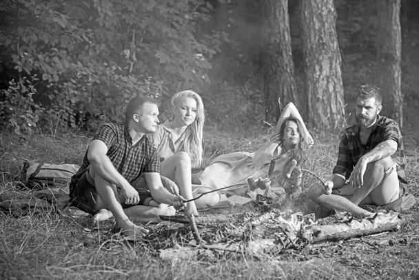 Young couples in love having picnic in woods, double date. Bearded man and his friend frying sausages over campfire, friendship and leisure concept - Fotoğraf, Görsel