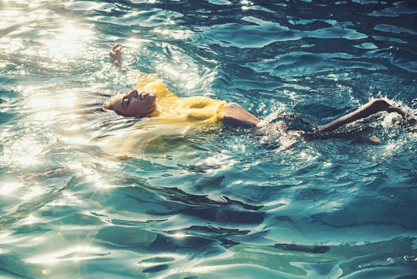 Beautiful young woman in sexy yellow dress swimming at sea beach - Photo, image