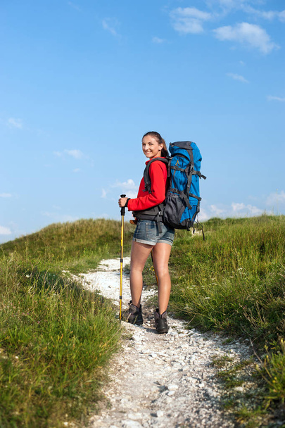 Smiling woman with backpack and trekking poles on the mountain t - Valokuva, kuva