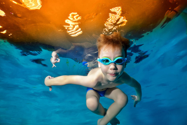 Спортивный мальчик плавает под водой в бассейне. Поза для камеры в очках для плавания. Вид снизу со дна бассейна. Портрет. Подводная фотография. Горизонтальный вид
 - Фото, изображение