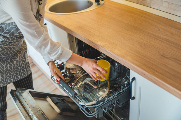 Молодая красивая женщина кладет посуду в посудомоечную машину
 - Фото, изображение
